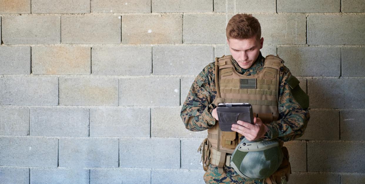 Soldat mit Tablet-Computer vor einer alten Backsteinmauer