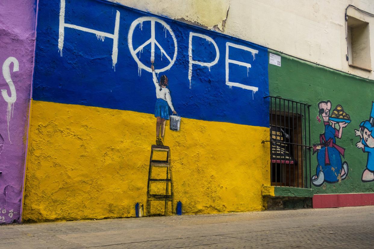 A little girl in front of the Ukrainian colors writing the word HOPE