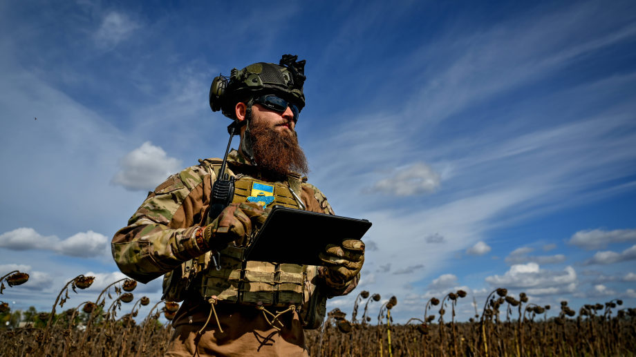 A soldier of a military mortar crew checks the direction on the tablet as he stands on the border of a dry sunflower field
