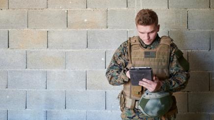 Soldat mit Tablet-Computer vor einer alten Backsteinmauer